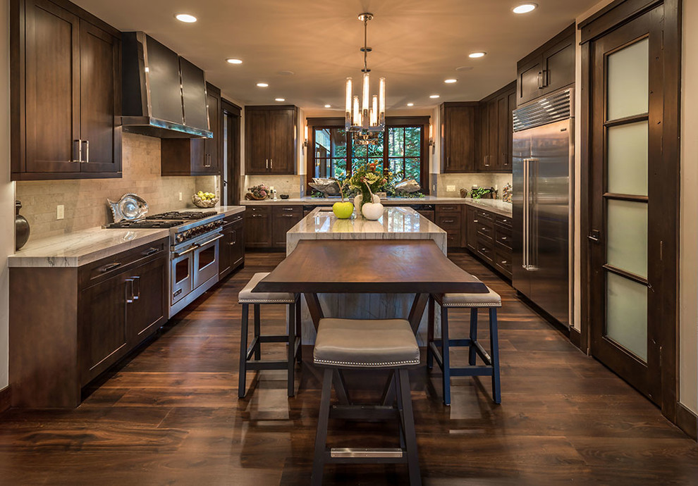 Photo of a country kitchen in Sacramento with shaker cabinets, dark wood cabinets, beige splashback, stainless steel appliances, dark hardwood floors, brown floor and multiple islands.
