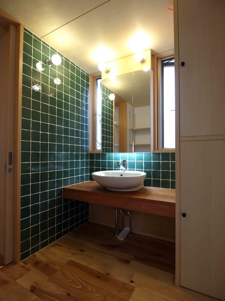 Design ideas for a small transitional powder room in Tokyo with green tile, white walls, medium hardwood floors, a vessel sink, wood benchtops, beaded inset cabinets, beige cabinets and brown benchtops.
