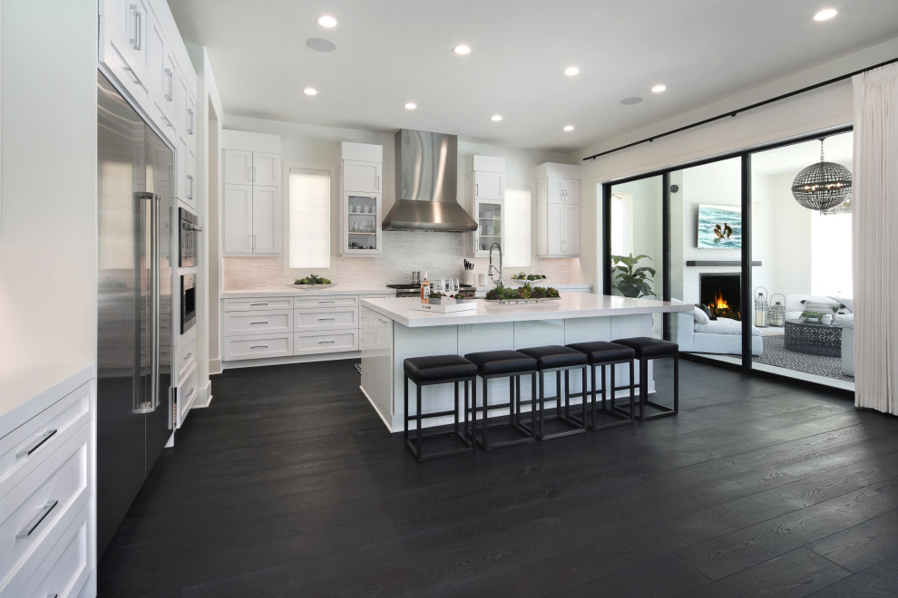 Inspiration for a large modern single-wall dark wood floor and black floor eat-in kitchen remodel in Orange County with a farmhouse sink, shaker cabinets, white cabinets, granite countertops, white backsplash, marble backsplash, stainless steel appliances, an island and white countertops