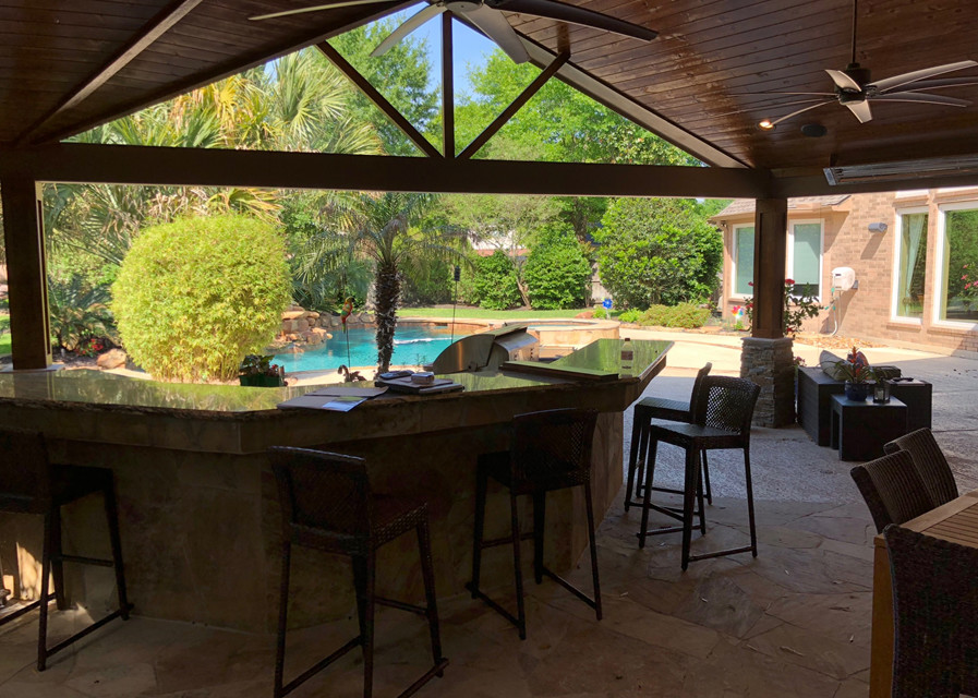 Photo of an expansive transitional backyard patio in Houston with an outdoor kitchen, natural stone pavers and a roof extension.