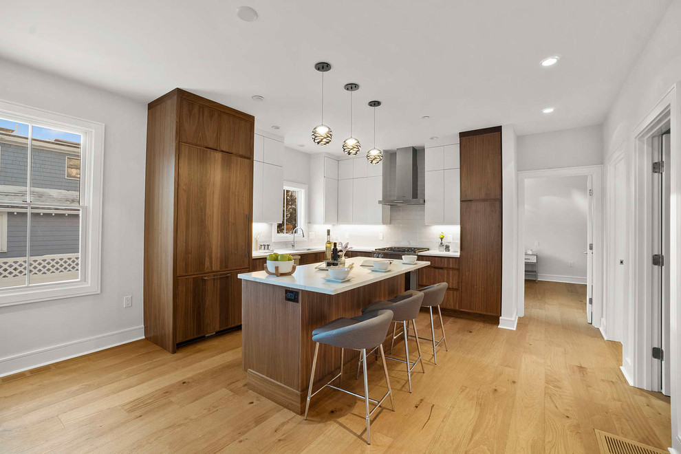 Mid-sized modern l-shaped eat-in kitchen in Boston with a drop-in sink, flat-panel cabinets, quartzite benchtops, white splashback, ceramic splashback, stainless steel appliances, medium hardwood floors, with island, brown floor, white benchtop and medium wood cabinets.