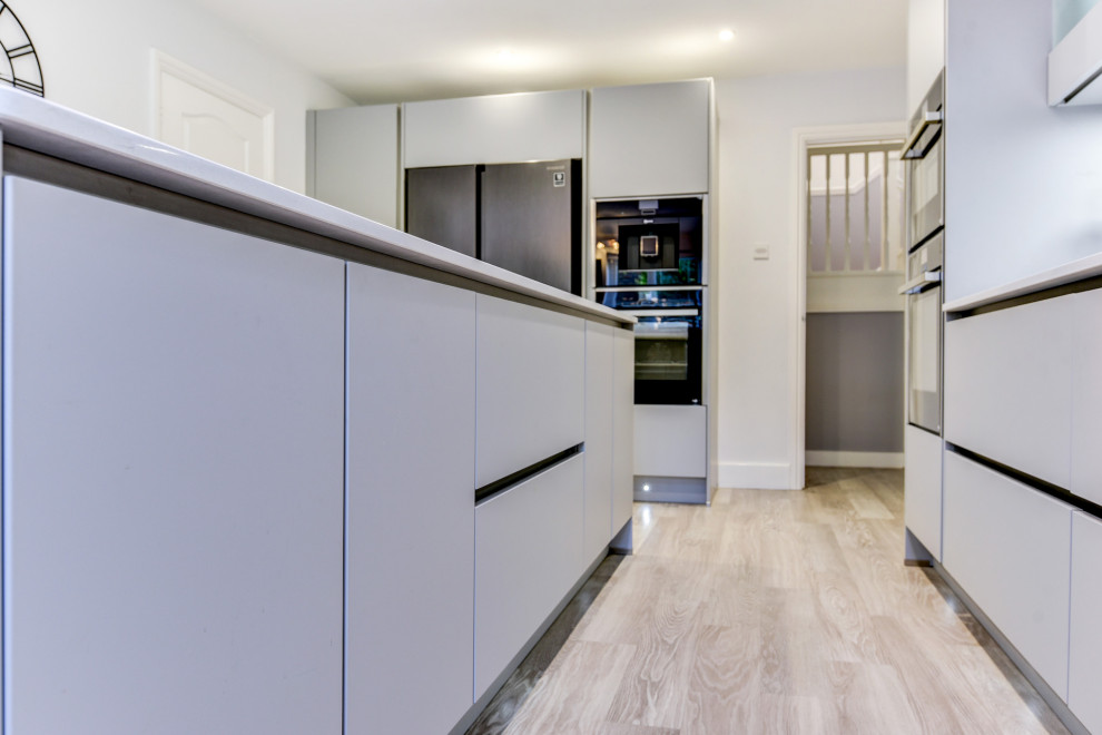 Photo of a large modern l-shaped eat-in kitchen in Sussex with an undermount sink, flat-panel cabinets, grey cabinets, quartzite benchtops, black splashback, glass sheet splashback, black appliances, vinyl floors, with island, grey floor and white benchtop.