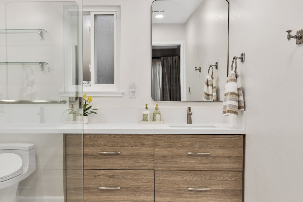This is an example of a small modern 3/4 bathroom in Phoenix with flat-panel cabinets, brown cabinets, an alcove shower, a two-piece toilet, grey walls, ceramic floors, engineered quartz benchtops, grey floor, a hinged shower door, white benchtops, a double vanity, a floating vanity, an undermount sink, brick walls, ceramic tile and gray tile.