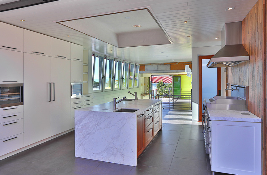 Photo of a large beach style galley eat-in kitchen in Los Angeles with an undermount sink, flat-panel cabinets, white cabinets, marble benchtops, multi-coloured splashback, stainless steel appliances, with island, timber splashback, concrete floors, grey floor and grey benchtop.