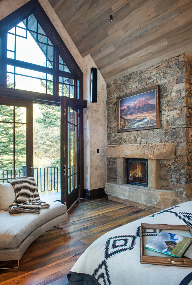 This is an example of a large country master bedroom in Other with beige walls, dark hardwood floors, a standard fireplace and a stone fireplace surround.