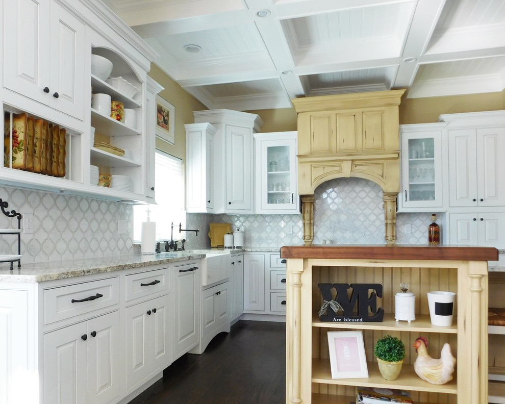This is an example of a large vintage l-shaped kitchen/diner in Denver with a belfast sink, raised-panel cabinets, white cabinets, granite worktops, white splashback, marble splashback, stainless steel appliances, dark hardwood flooring, an island, brown floors, grey worktops and a coffered ceiling.
