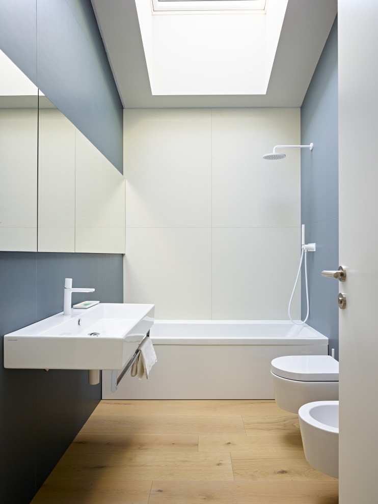 Exempel på ett skandinaviskt badrum, med luckor med glaspanel, vita skåp, ett platsbyggt badkar, en vägghängd toalettstol, blå kakel, grå väggar, mellanmörkt trägolv, ett väggmonterat handfat och beiget golv