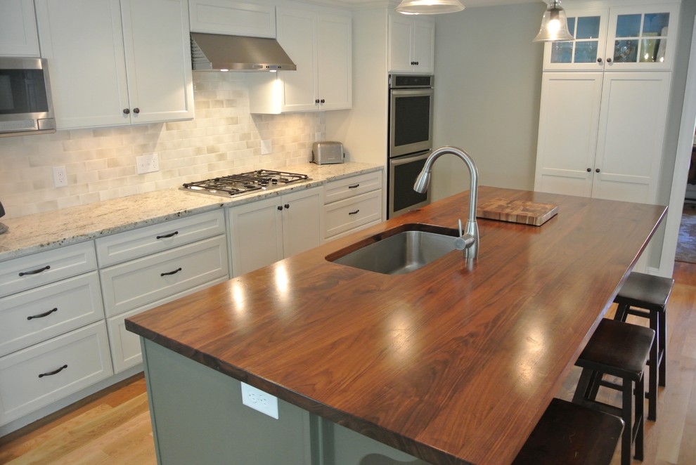 Example of a transitional galley light wood floor eat-in kitchen design in Boston with an undermount sink, shaker cabinets, white cabinets, wood countertops, white backsplash, ceramic backsplash, stainless steel appliances, an island and brown countertops