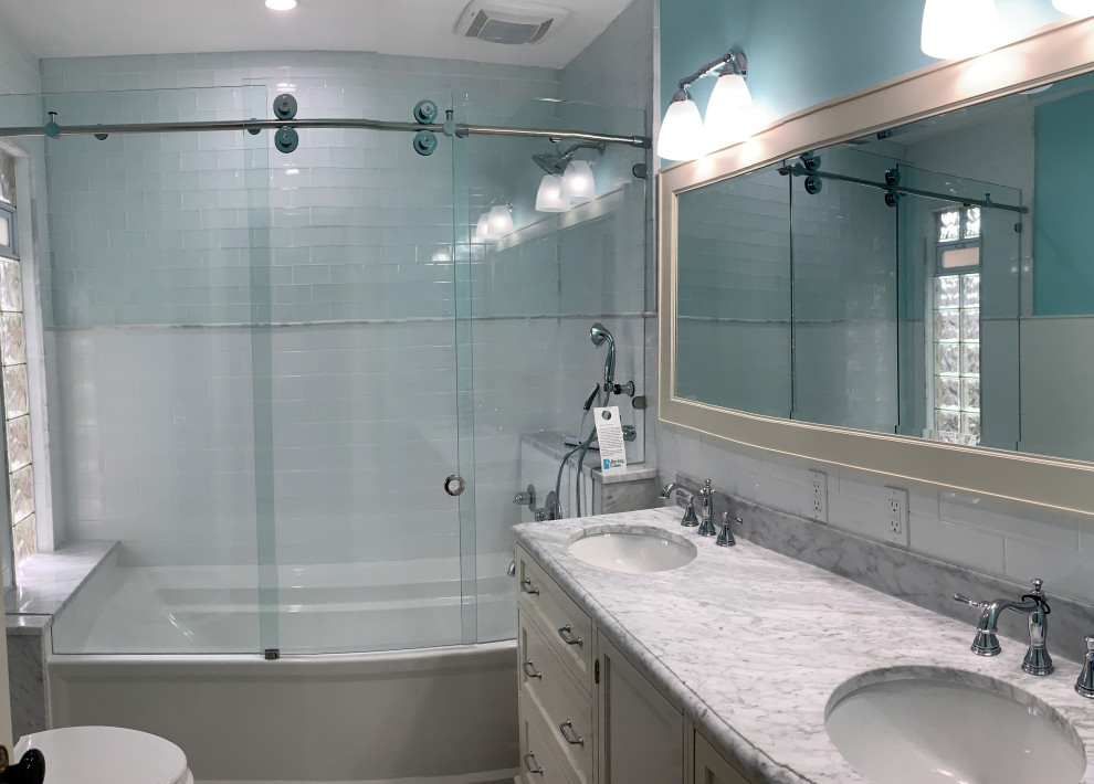 Foto på ett stort vintage vit en-suite badrum, med möbel-liknande, vita skåp, ett badkar i en alkov, en dusch/badkar-kombination, en toalettstol med separat cisternkåpa, vit kakel, glaskakel, blå väggar, klinkergolv i keramik, ett undermonterad handfat, marmorbänkskiva, grått golv och dusch med skjutdörr
