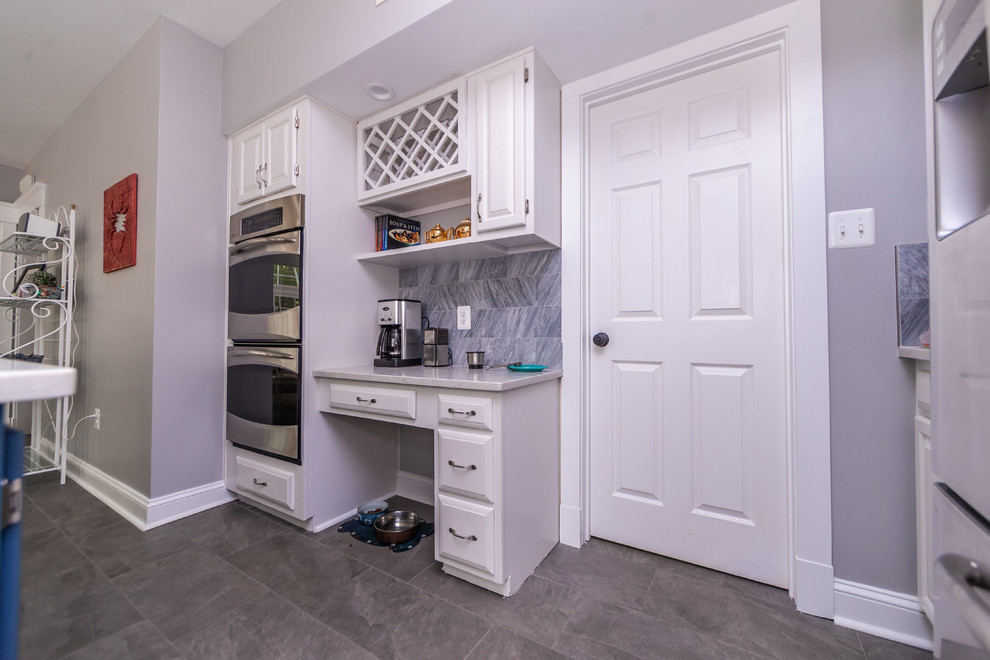This is an example of a large transitional u-shaped kitchen pantry in Baltimore with an undermount sink, raised-panel cabinets, white cabinets, quartz benchtops, grey splashback, stainless steel appliances, porcelain floors, with island, grey floor and white benchtop.