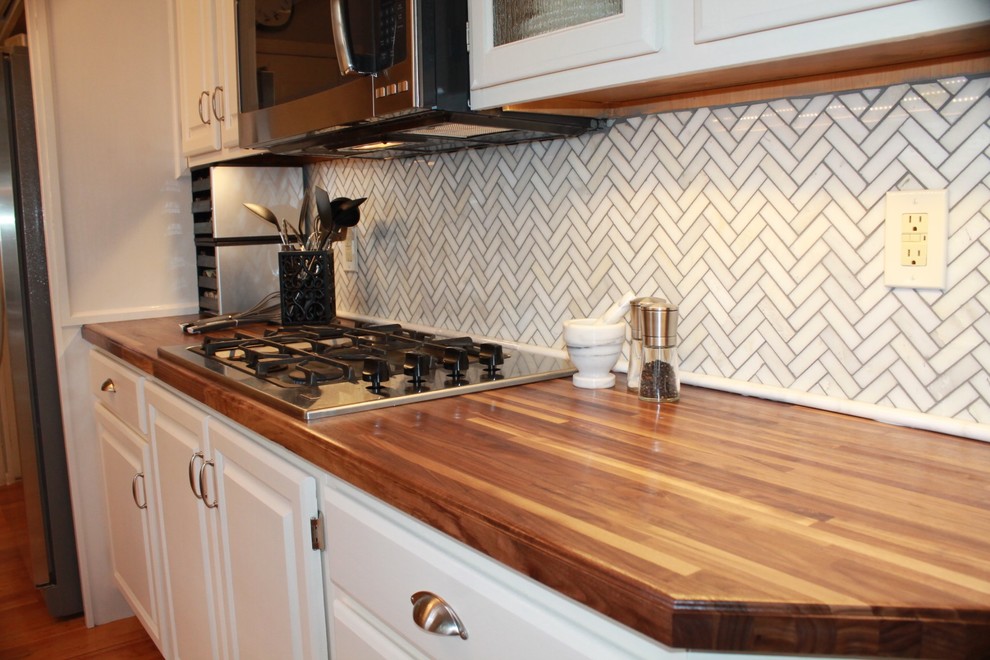 Eat-in kitchen - mid-sized transitional galley light wood floor eat-in kitchen idea with an undermount sink, raised-panel cabinets, white cabinets, wood countertops, white backsplash, stone tile backsplash, stainless steel appliances and no island