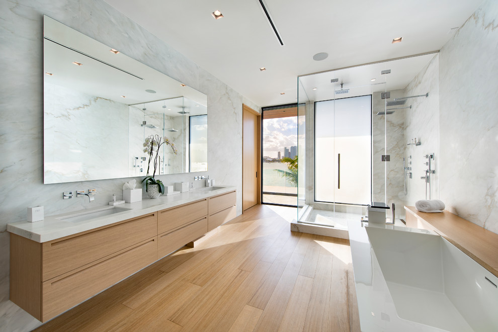 Large contemporary master bathroom in Miami with flat-panel cabinets, beige cabinets, a freestanding tub, a double shower, a wall-mount toilet, white tile, stone slab, white walls, light hardwood floors, an undermount sink, marble benchtops, beige floor, a hinged shower door and yellow benchtops.