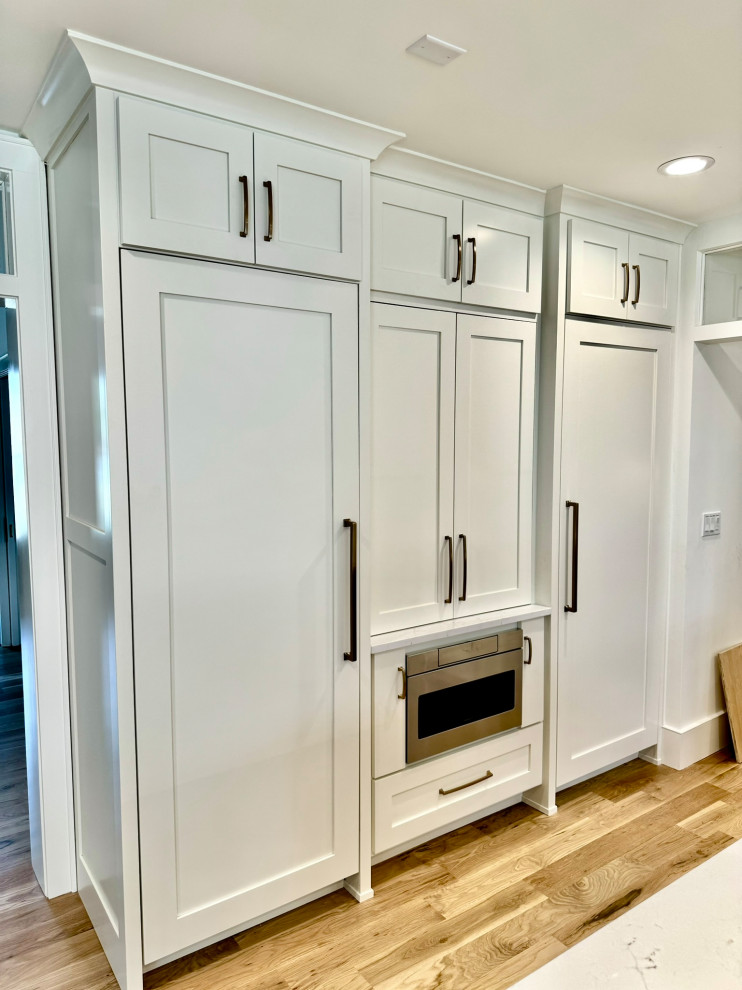 Example of a mid-sized transitional l-shaped light wood floor, brown floor and wallpaper ceiling eat-in kitchen design in Atlanta with a farmhouse sink, shaker cabinets, white cabinets, granite countertops, white backsplash, stainless steel appliances, an island and white countertops