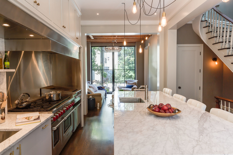 Example of a transitional galley medium tone wood floor kitchen design with an undermount sink, flat-panel cabinets, white cabinets, marble countertops, stainless steel appliances and an island