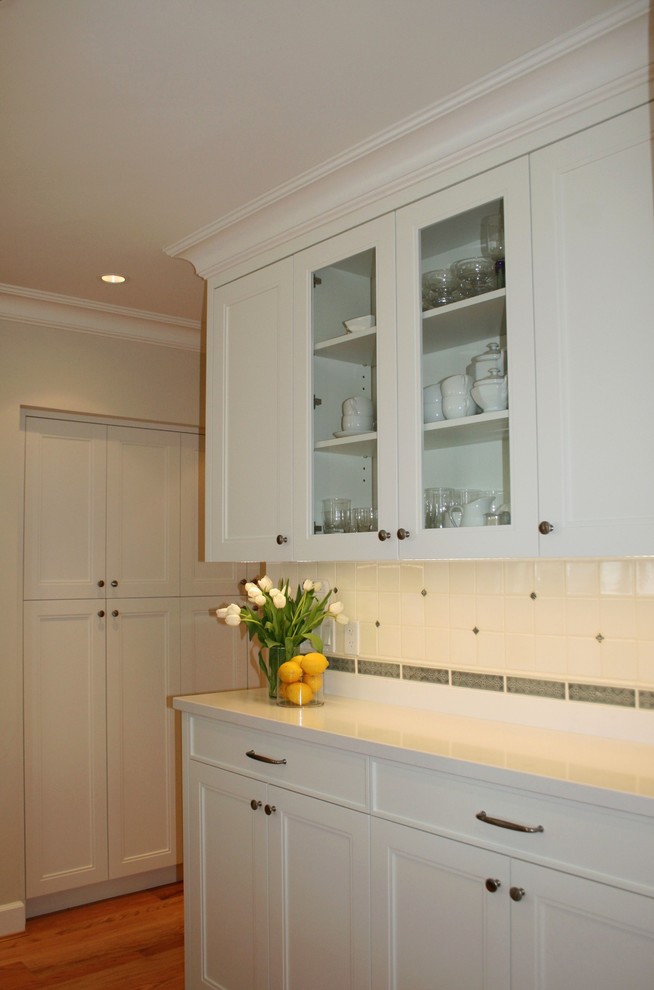 Photo of a large traditional kitchen pantry in Vancouver with an undermount sink, recessed-panel cabinets, white cabinets, granite benchtops, white splashback, ceramic splashback, panelled appliances, light hardwood floors and with island.