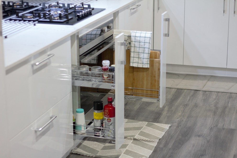 Photo of a modern eat-in kitchen in Perth with white cabinets, quartz benchtops, grey splashback, glass tile splashback, black appliances, medium hardwood floors, with island and grey floor.