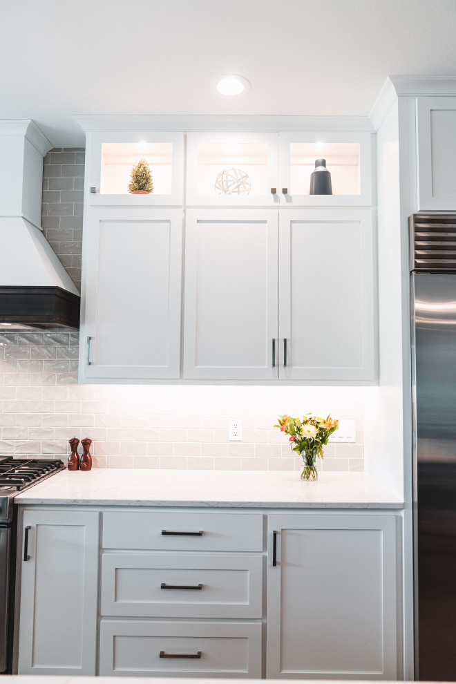 Kitchen pantry - large transitional l-shaped vinyl floor and brown floor kitchen pantry idea with an undermount sink, shaker cabinets, white cabinets, quartz countertops, gray backsplash, subway tile backsplash, stainless steel appliances, an island and white countertops