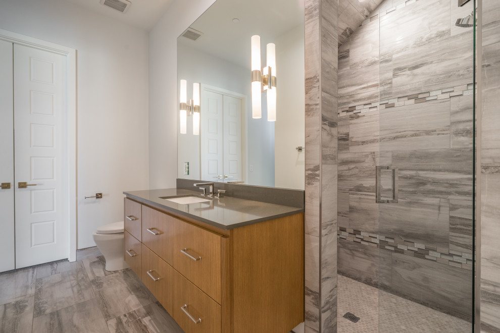 Mid-sized contemporary 3/4 bathroom in Dallas with flat-panel cabinets, light wood cabinets, a one-piece toilet, gray tile, porcelain tile, white walls, porcelain floors, an undermount sink, engineered quartz benchtops, grey floor, a hinged shower door, grey benchtops, a single vanity and a floating vanity.