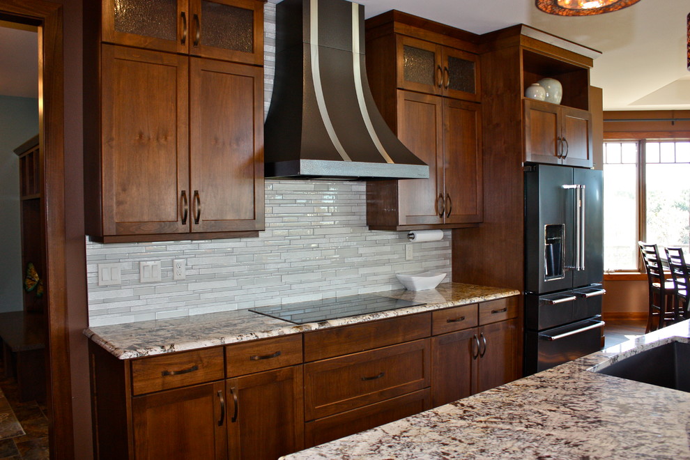 Open concept kitchen - large transitional l-shaped medium tone wood floor and brown floor open concept kitchen idea with an undermount sink, recessed-panel cabinets, medium tone wood cabinets, granite countertops, white backsplash, glass tile backsplash, stainless steel appliances and an island