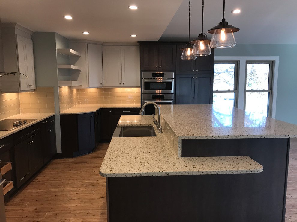 Photo of a mid-sized transitional l-shaped kitchen pantry in Raleigh with a farmhouse sink, yellow splashback, glass tile splashback, stainless steel appliances, bamboo floors, with island, flat-panel cabinets, black cabinets, marble benchtops, brown floor and multi-coloured benchtop.