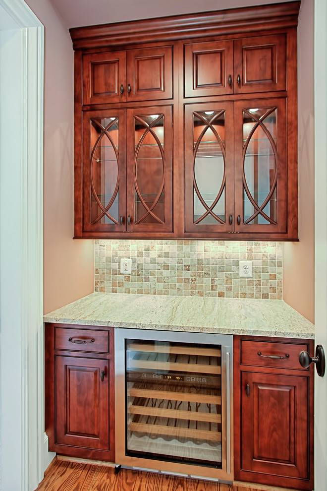 This is an example of a small traditional single-wall wet bar in DC Metro with no sink, raised-panel cabinets, dark wood cabinets, marble benchtops, multi-coloured splashback, mosaic tile splashback, dark hardwood floors and brown floor.
