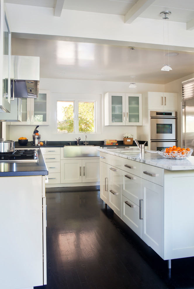 Photo of a transitional l-shaped open plan kitchen in Los Angeles with a farmhouse sink, shaker cabinets, white cabinets, dark hardwood floors and with island.