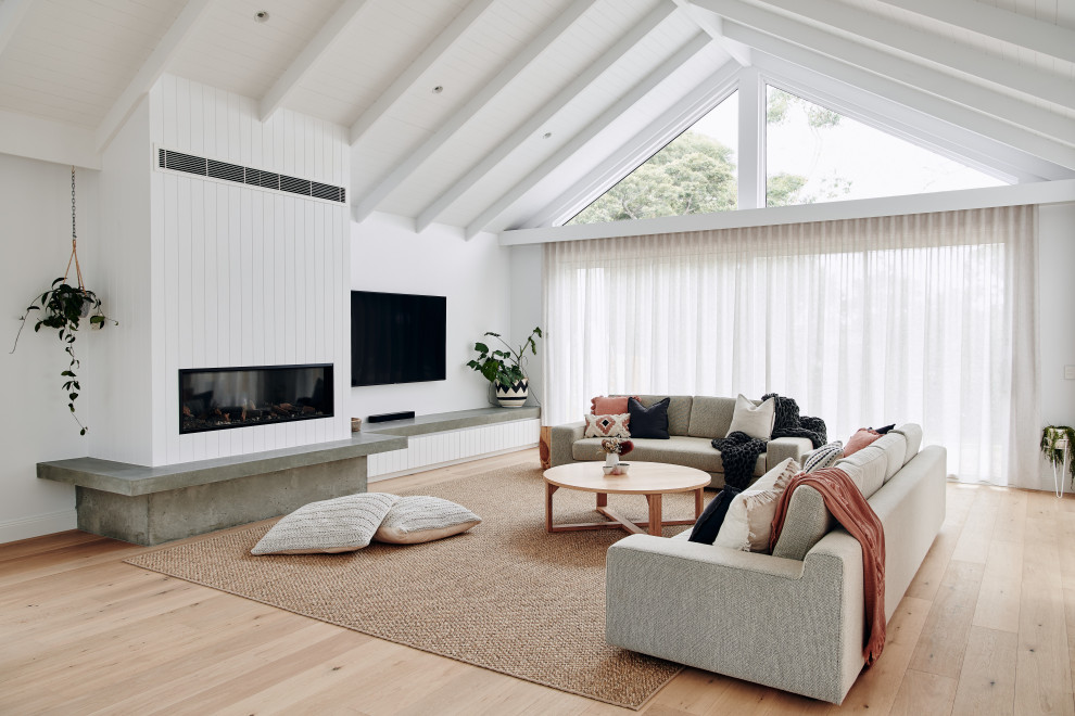 This is an example of a large contemporary open concept living room in Melbourne with white walls, light hardwood floors, a standard fireplace, a plaster fireplace surround, a wall-mounted tv, beige floor, recessed and panelled walls.