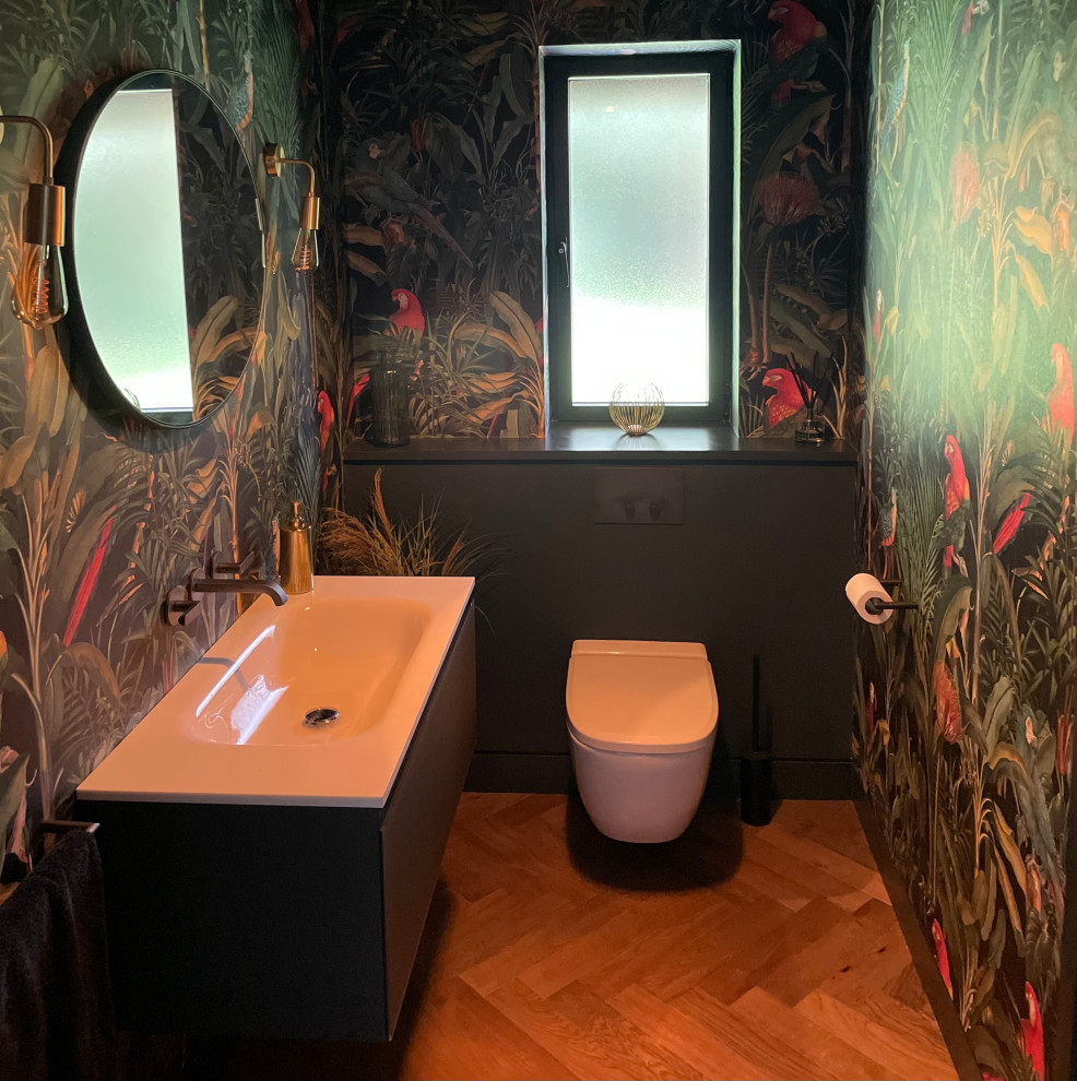 Cette image montre un petit WC suspendu design avec des portes de placard grises, un mur multicolore, parquet clair, un lavabo suspendu, un sol marron, meuble-lavabo suspendu et du papier peint.