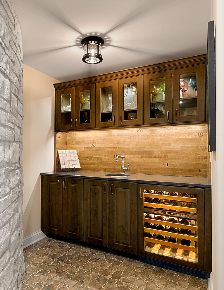 Design ideas for a mid-sized mediterranean single-wall wet bar in Chicago with an undermount sink, raised-panel cabinets, dark wood cabinets, granite benchtops, brown splashback, timber splashback, ceramic floors and brown floor.
