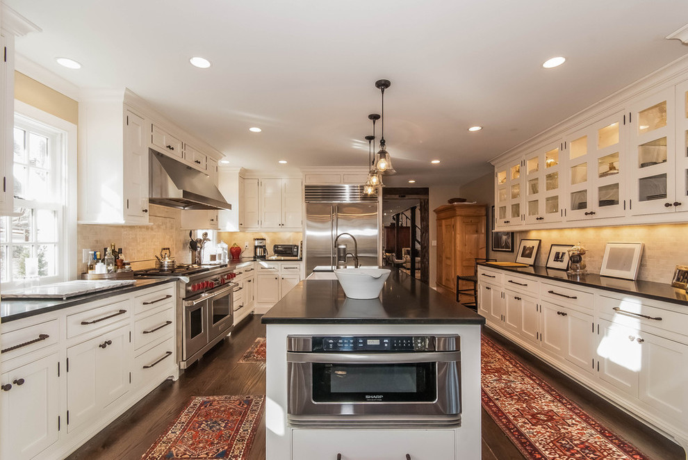 Inspiration for a large transitional u-shaped dark wood floor and brown floor open concept kitchen remodel in New York with recessed-panel cabinets, white cabinets, beige backsplash, stainless steel appliances, an island, a farmhouse sink, granite countertops, stone tile backsplash and black countertops