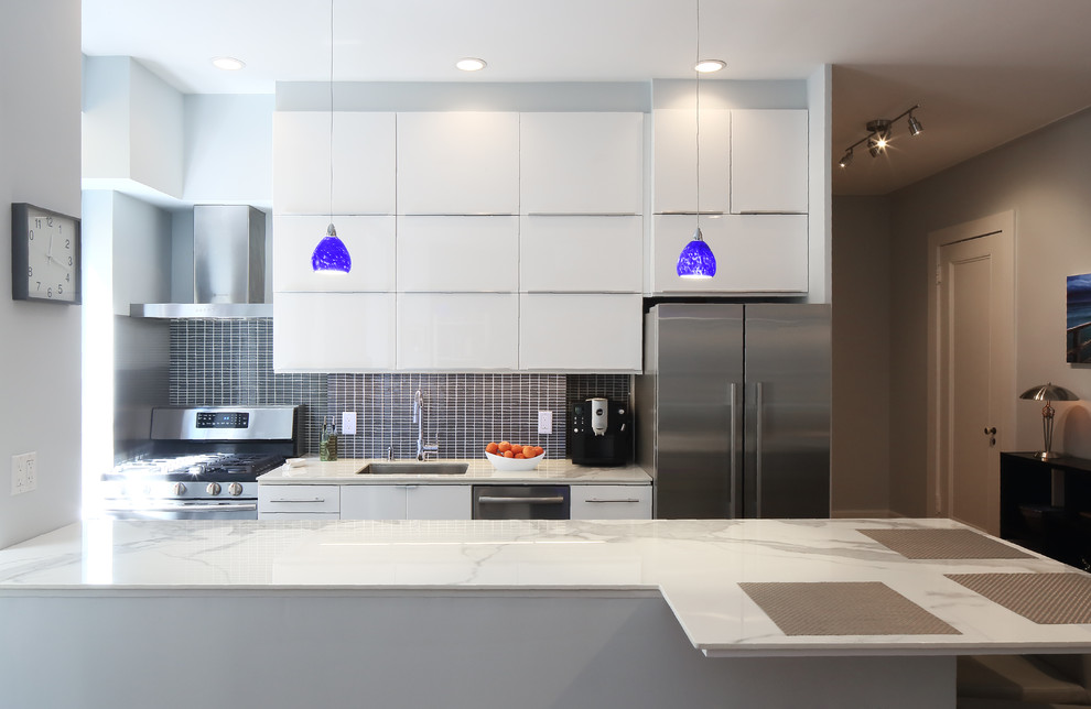 This is an example of a small contemporary galley open plan kitchen in New York with an undermount sink, flat-panel cabinets, white cabinets, blue splashback, glass tile splashback, stainless steel appliances, linoleum floors and a peninsula.