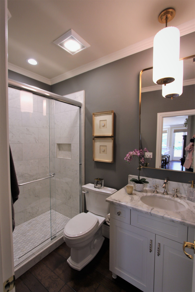 This is an example of a mid-sized transitional 3/4 bathroom in San Francisco with raised-panel cabinets, white cabinets, an alcove shower, a two-piece toilet, white tile, porcelain tile, grey walls, dark hardwood floors, an undermount sink, marble benchtops, brown floor, a sliding shower screen, white benchtops, a niche, a single vanity and a built-in vanity.