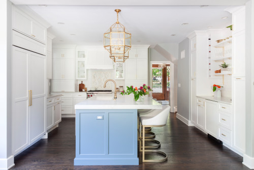 Bright white kitchen with shaker RTA cabinets, brass hardware, panel-ready fridge, blue island with waterfall quartz top, gold lantern pendant, and open shelves.