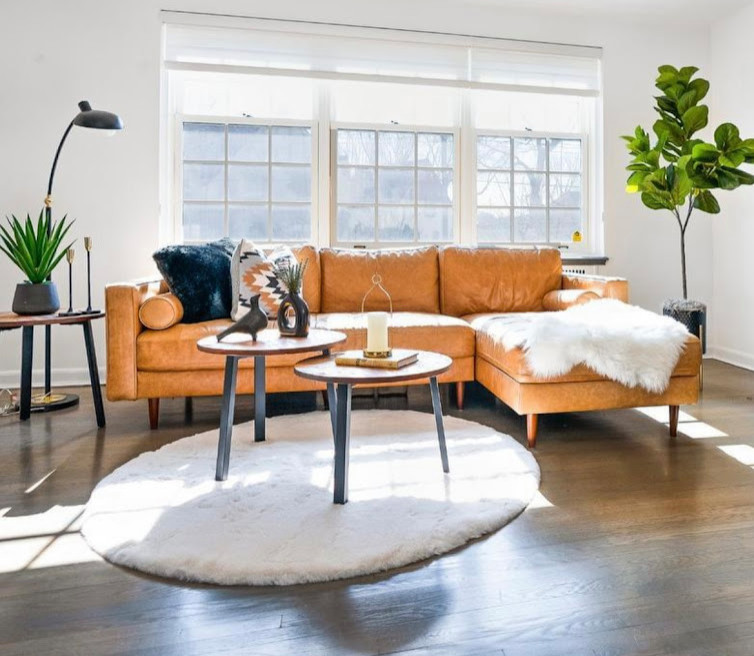 Modelo de salón abierto grande con paredes blancas, suelo de madera oscura, estufa de leña, televisor colgado en la pared y suelo marrón