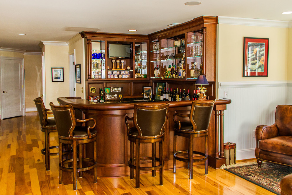 This is an example of a mid-sized traditional u-shaped seated home bar in Richmond with recessed-panel cabinets, dark wood cabinets, wood benchtops, medium hardwood floors and brown benchtop.