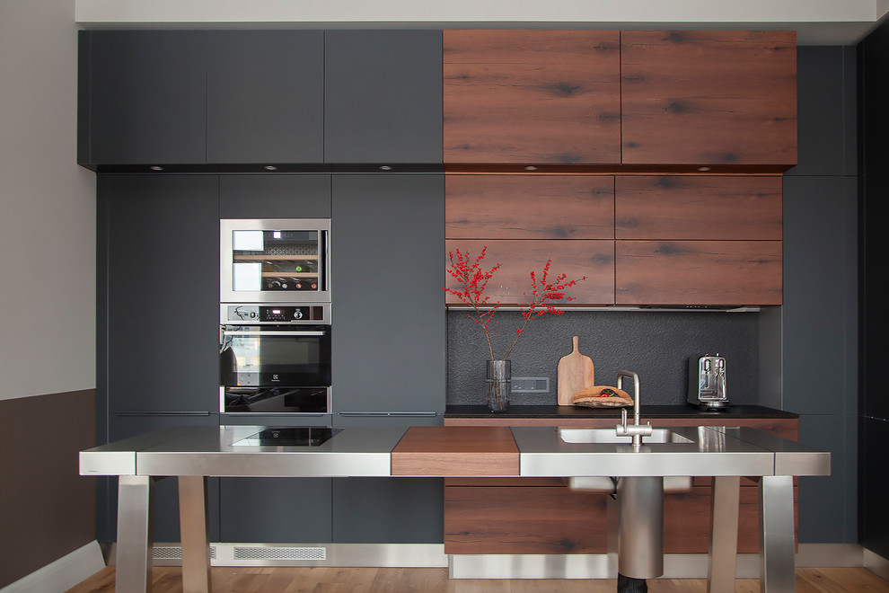 Mid-sized contemporary single-wall eat-in kitchen in Other with flat-panel cabinets, black cabinets, granite benchtops, black splashback, stone slab splashback, stainless steel appliances, medium hardwood floors, with island, black benchtop, an integrated sink and brown floor.