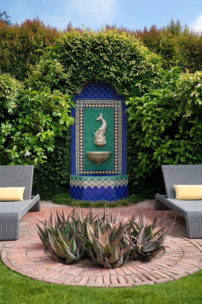 This is an example of a mediterranean patio in Santa Barbara with a water feature, brick pavers and no cover.