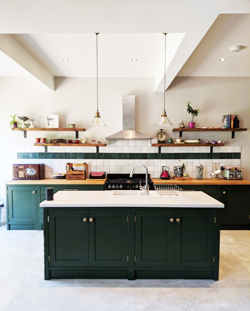 This is an example of a mid-sized traditional galley eat-in kitchen in London with a double-bowl sink, shaker cabinets, green cabinets, white splashback, ceramic splashback, black appliances, with island, wood benchtops, grey floor and brown benchtop.