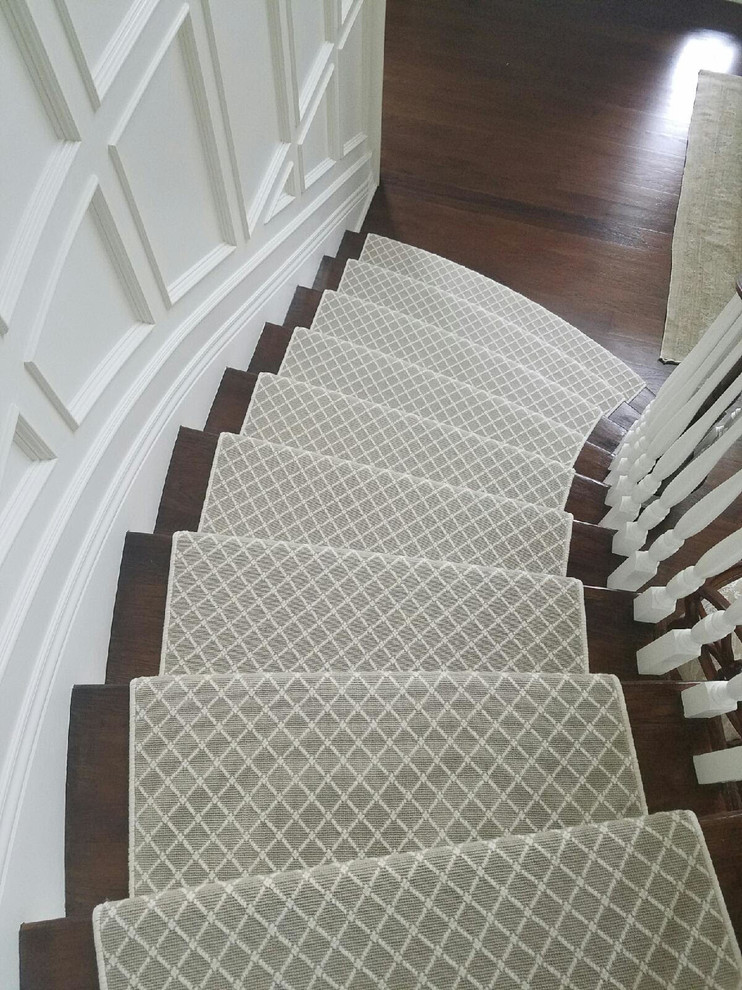 Imagen de escalera curva clásica grande con escalones de madera, contrahuellas de madera pintada y barandilla de madera