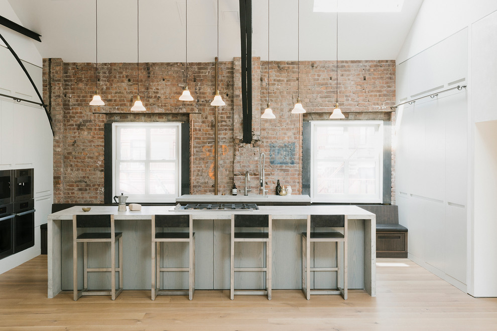 This is an example of an industrial kitchen in New York with light hardwood floors and with island.