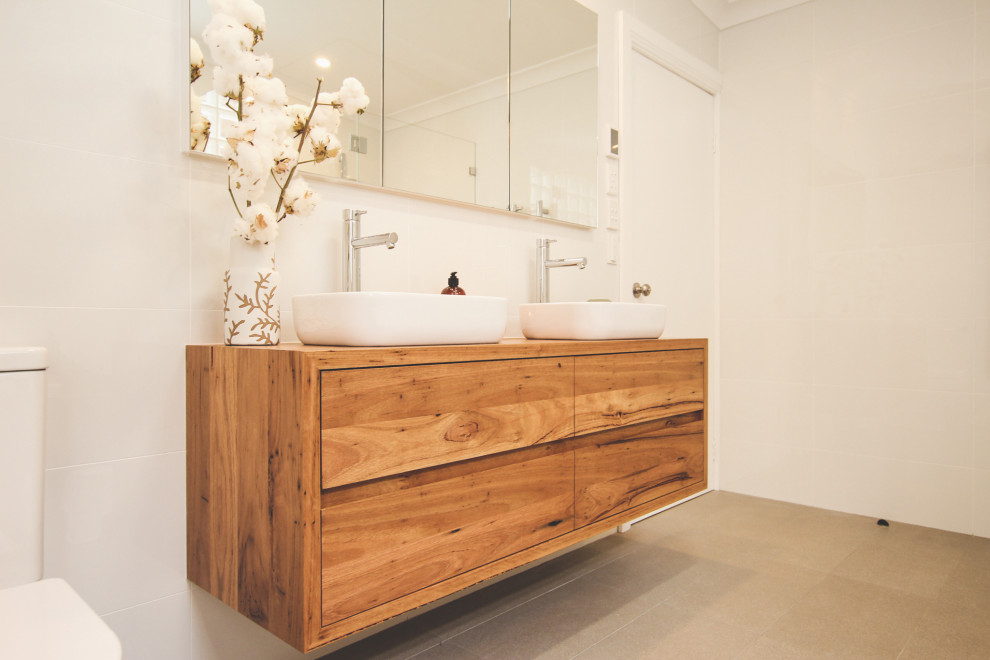 This is an example of a large contemporary ensuite bathroom in Sydney with medium wood cabinets, a built-in bath, a double shower, white tiles, white walls, a vessel sink, wooden worktops, brown floors, a hinged door, a wall niche, double sinks and a floating vanity unit.