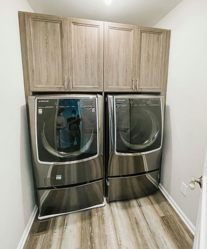 This is an example of a small contemporary galley dedicated laundry room in New York with beaded inset cabinets, beige cabinets, beige walls, laminate floors, a side-by-side washer and dryer and brown floor.