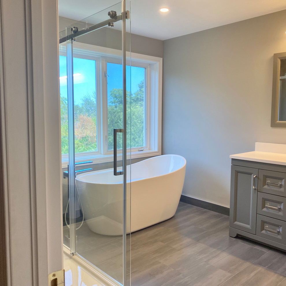 Inspiration for a huge transitional master porcelain tile porcelain tile, gray floor and single-sink freestanding bathtub remodel with recessed-panel cabinets, a one-piece toilet, an undermount sink, quartzite countertops, white countertops and a built-in vanity