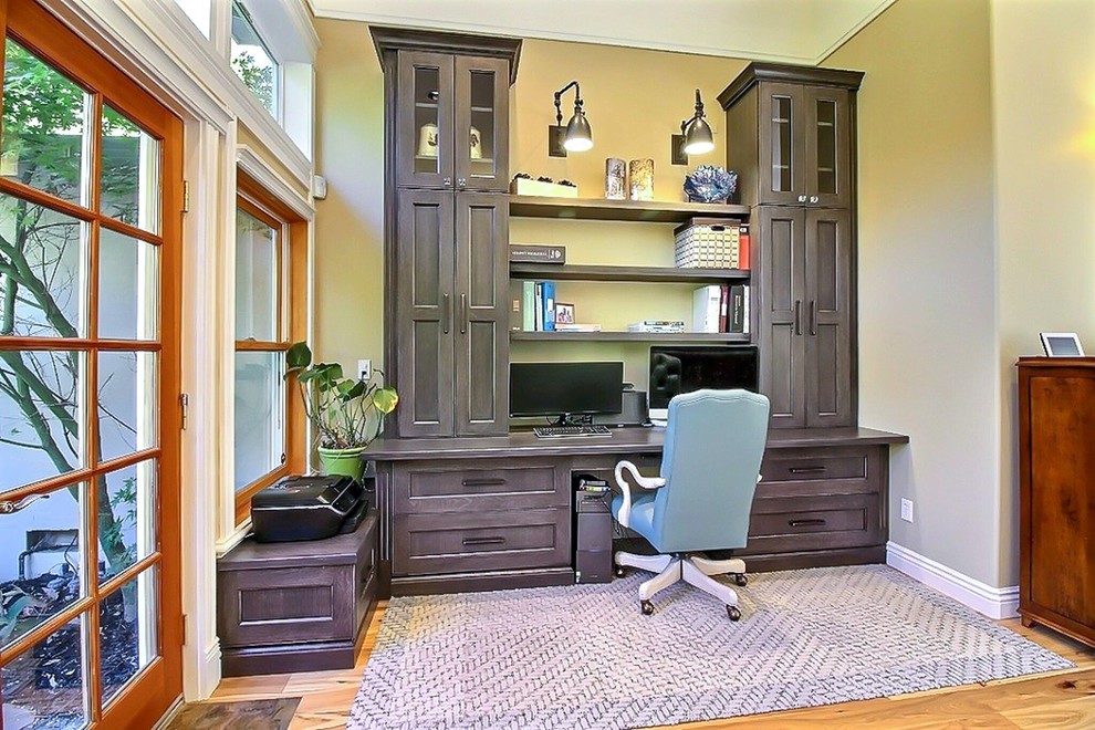 Photo of a large transitional study room in San Francisco with beige walls, light hardwood floors, a standard fireplace, a wood fireplace surround, a built-in desk and brown floor.