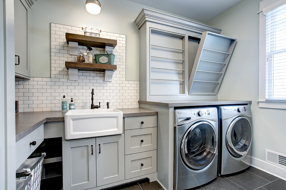 Photo of a transitional l-shaped dedicated laundry room in Grand Rapids with a farmhouse sink, shaker cabinets, grey cabinets, grey walls, a side-by-side washer and dryer, grey floor and grey benchtop.