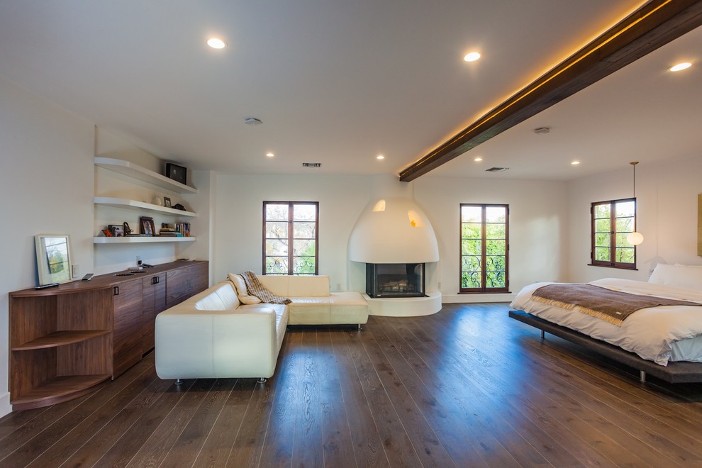 Photo of a mid-sized mediterranean master bedroom in Los Angeles with white walls, dark hardwood floors, a standard fireplace, a plaster fireplace surround and brown floor.