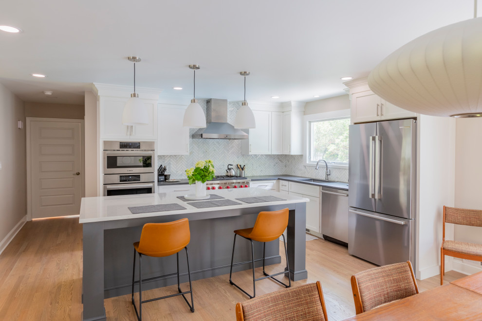 Photo of a large transitional l-shaped eat-in kitchen in New York with an undermount sink, shaker cabinets, white cabinets, quartz benchtops, white splashback, marble splashback, stainless steel appliances, medium hardwood floors, with island and white benchtop.