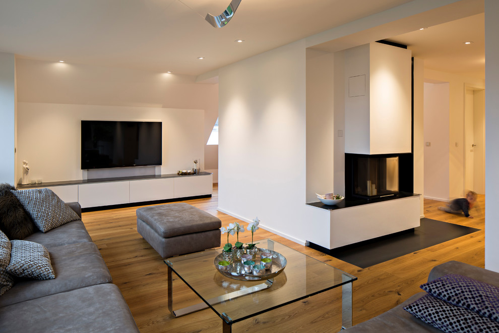 This is an example of a large contemporary open concept living room in Other with white walls, medium hardwood floors, a wall-mounted tv, a standard fireplace and a plaster fireplace surround.