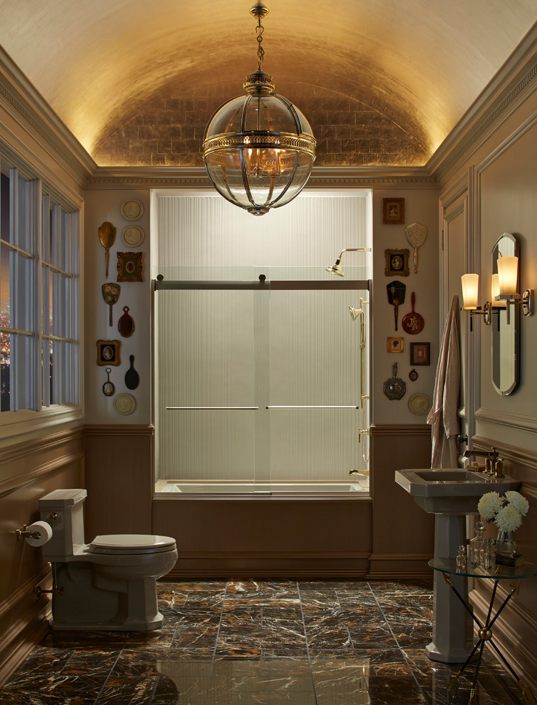 Inspiration for a mid-sized traditional master bathroom in Minneapolis with an alcove tub, a shower/bathtub combo, a two-piece toilet, brown tile, stone tile, beige walls, marble floors, a pedestal sink and solid surface benchtops.