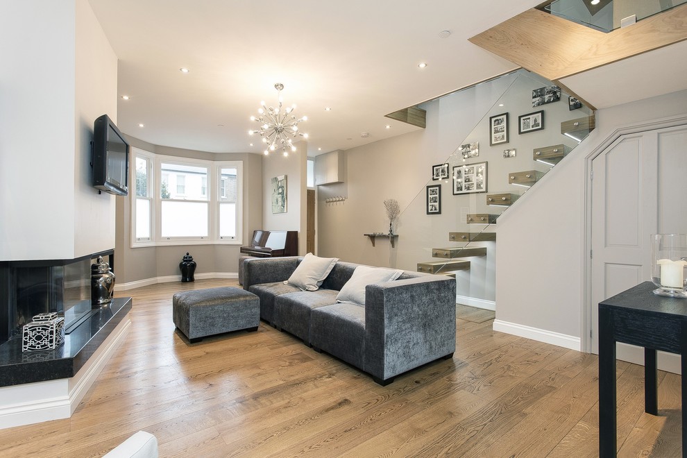 This is an example of a contemporary living room in Surrey with grey walls, medium hardwood floors and a wall-mounted tv.